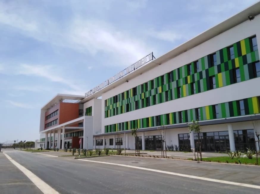 Façade de l'Hôpital Universitaire Mohammed VI, un bâtiment moderne blanc avec des motifs géométriques verts et jaunes vifs sur une aile, et des sections oranges sur l'autre, sous un ciel bleu clair.