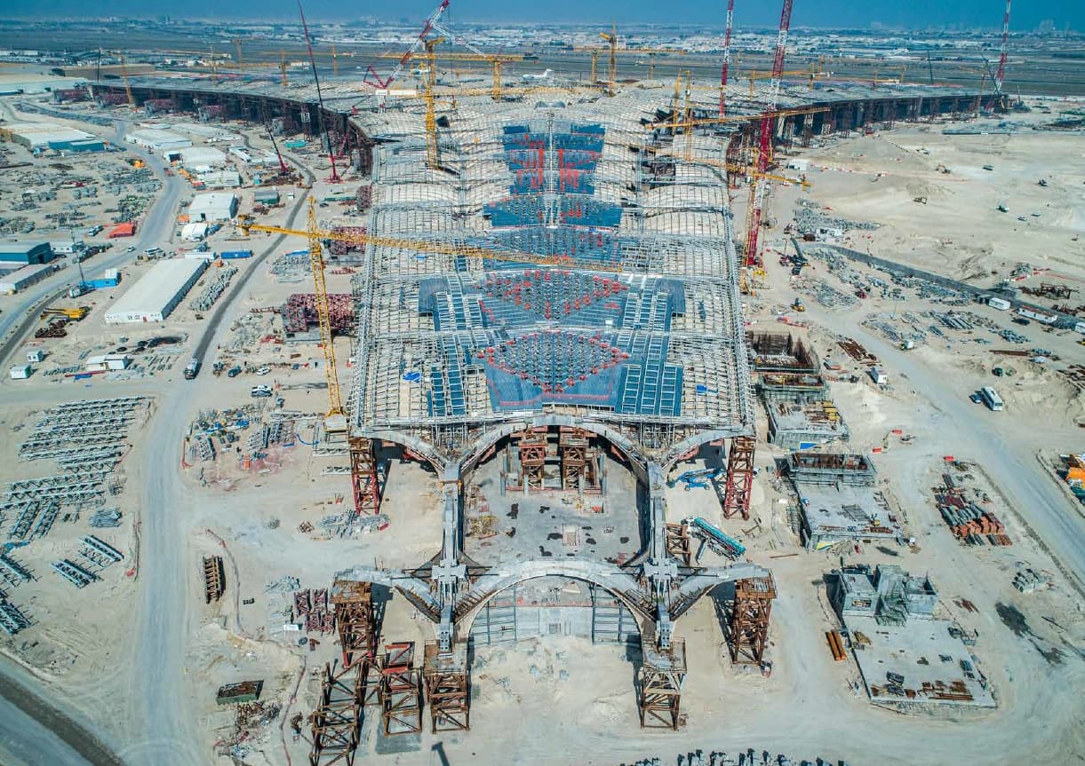 Vue aérienne d'un terminal d'aéroport en chantier, avec une imposante structure de toit en acier et de nombreuses grues.